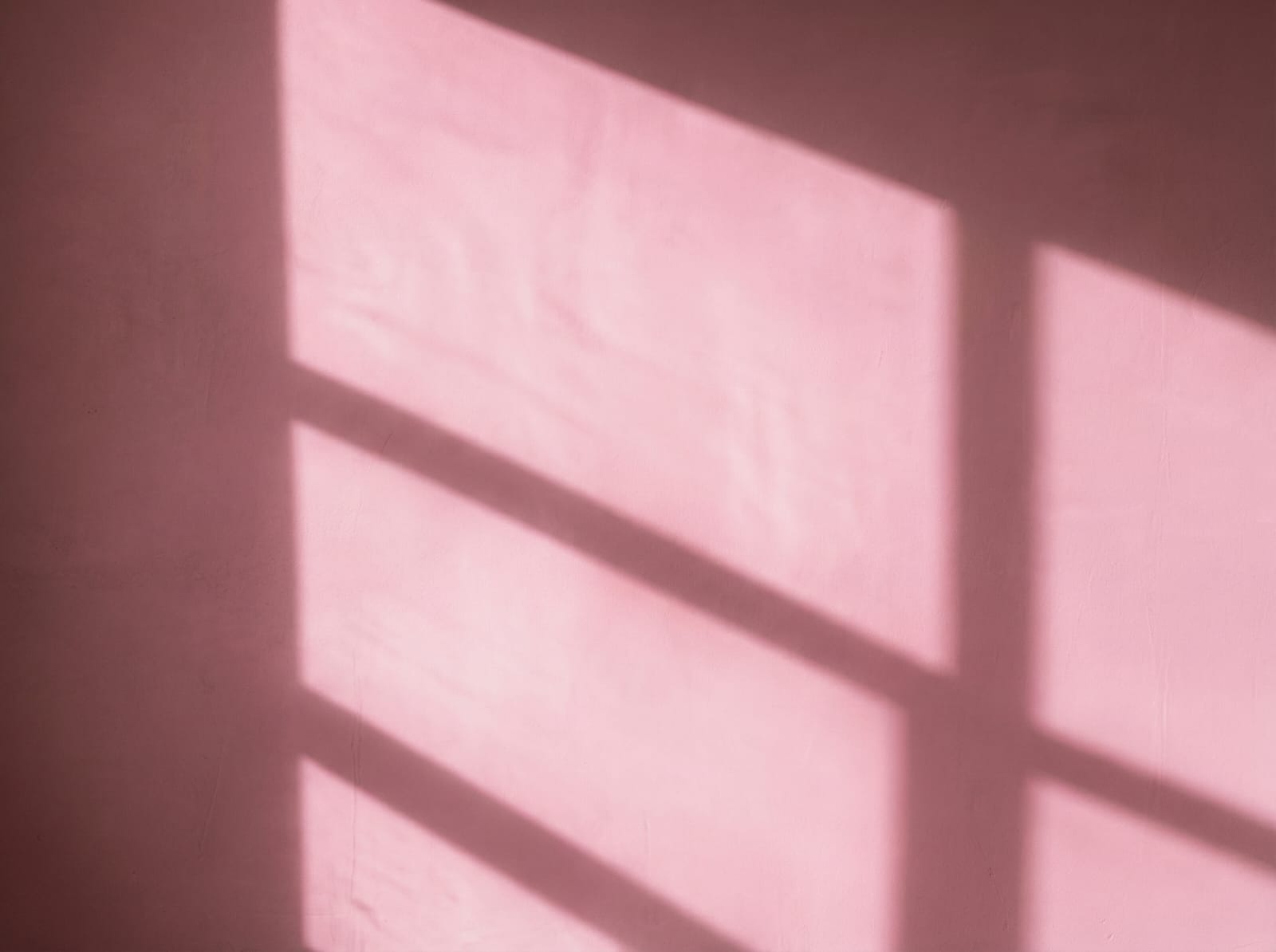 A textured, matte black wall with strong geometric shadows cast from an unseen light source, resembling window panes.