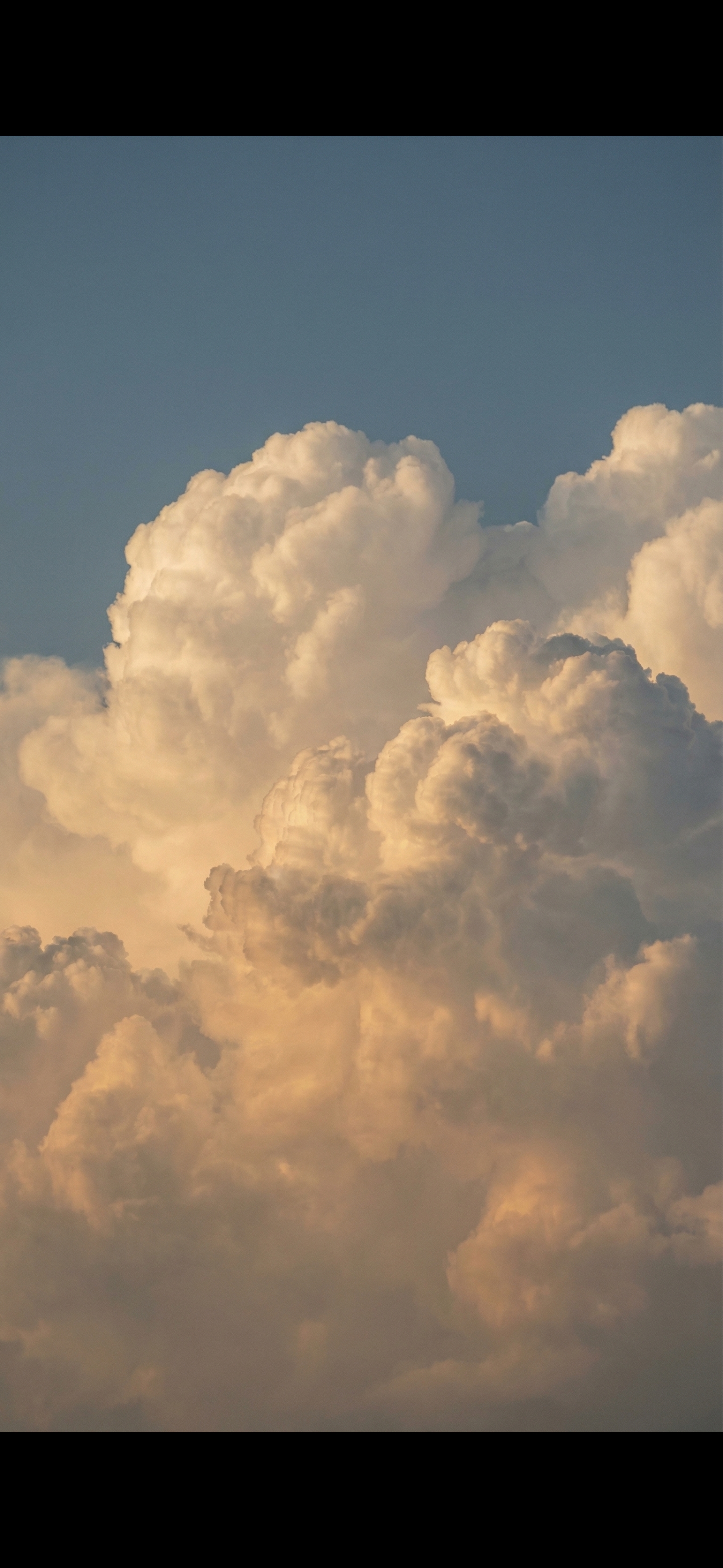 Vast expanse of a clear blue sky transitioning to dramatic, voluminous cumulus clouds illuminated by warm, directional light.